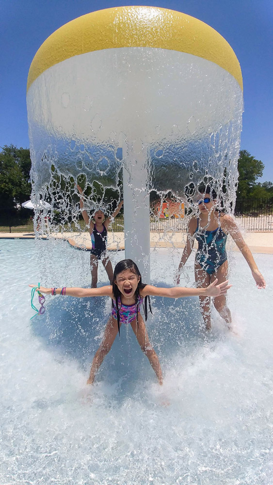 3 girls in swimsuits under an umbrella of water having fun