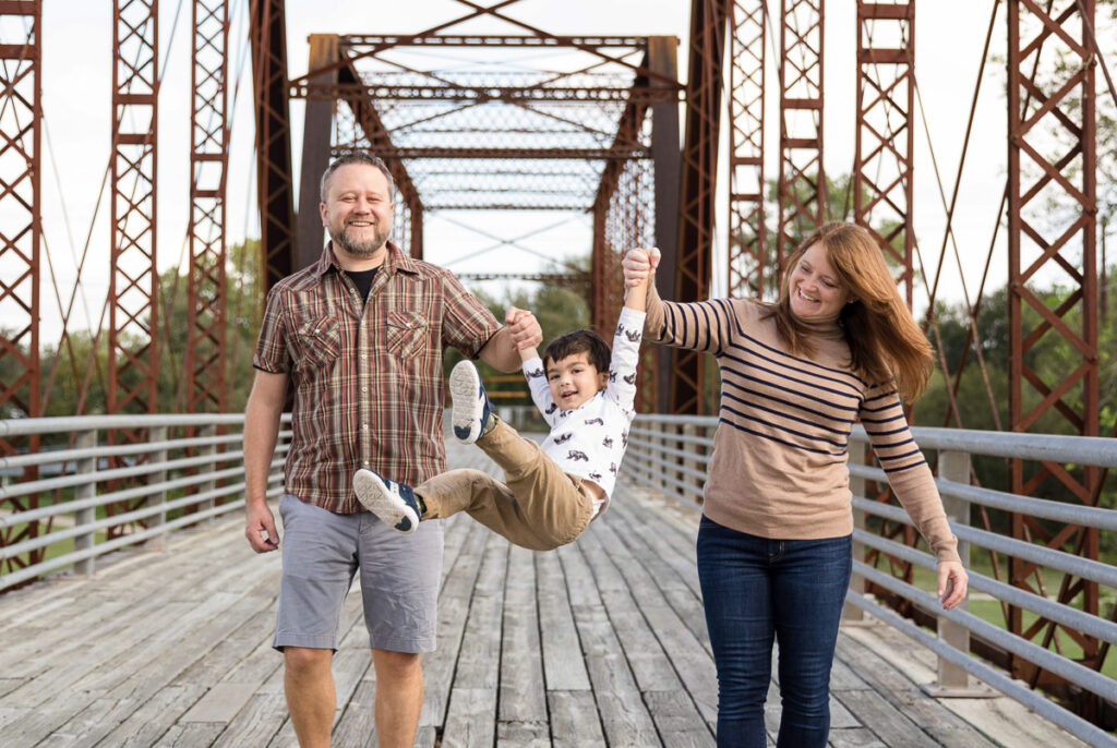 Family photo session on a bridge with parents swinging little boy between them