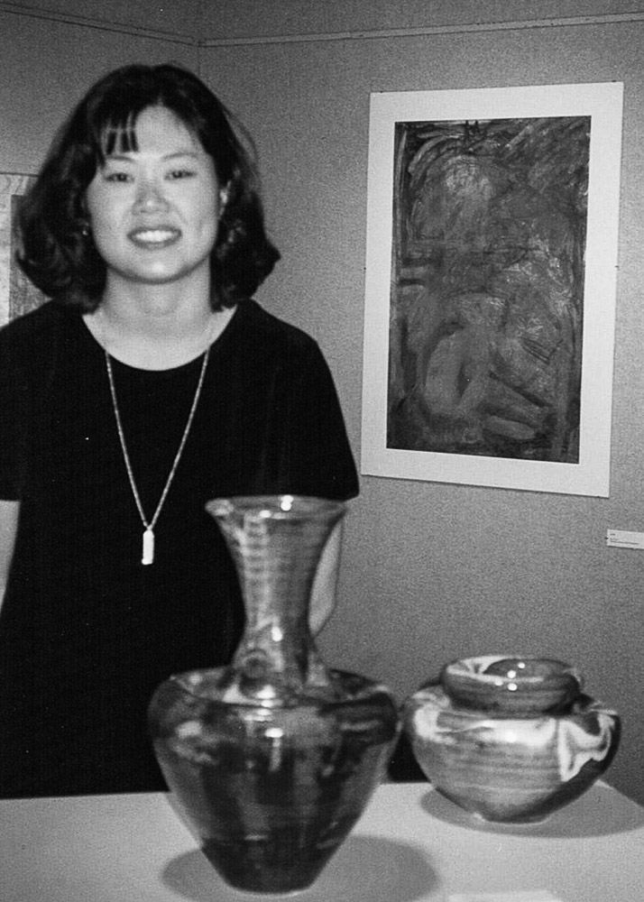 black and white of a woman at an art show with her wall art and ceramic pieces