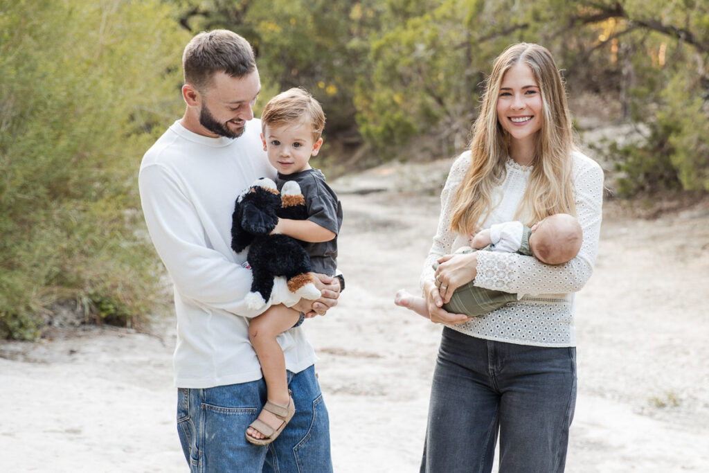Family walking together outdoors in Austin, Texas during a lifestyle family photography session with parents holding their young children.