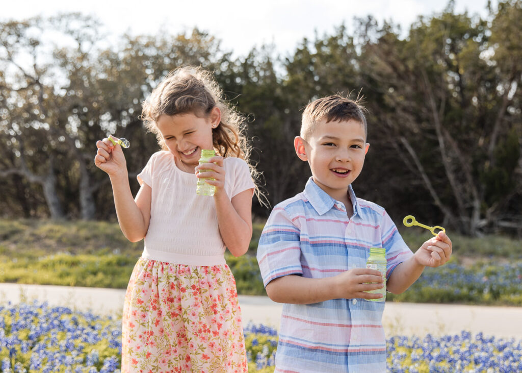 Two children playing with bubbles outdoors during a playful lifestyle family photography session in Austin, Texas.