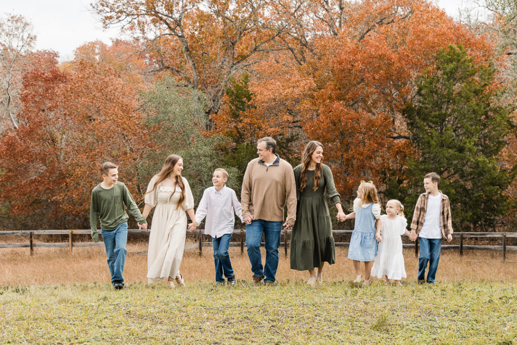 Large family walking together through a field during a fall lifestyle family photography session in Lockhart.