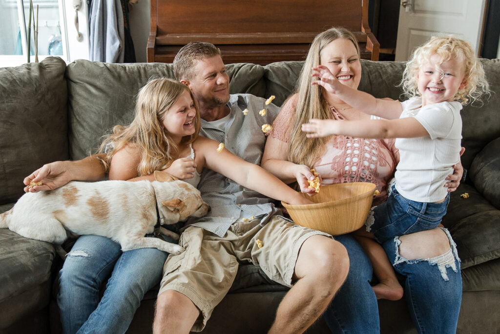 Family throwing popcorn at each other and laughing on the couch during a relaxed in-home lifestyle family photography session in Kyle.