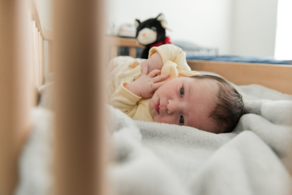 Awake newborn resting in crib during natural in-home newborn photography in Austin