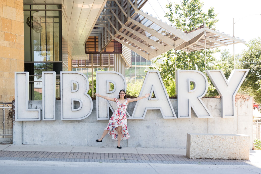 High school senior girl standing in front of the Austin Central Library sign during her senior portraits