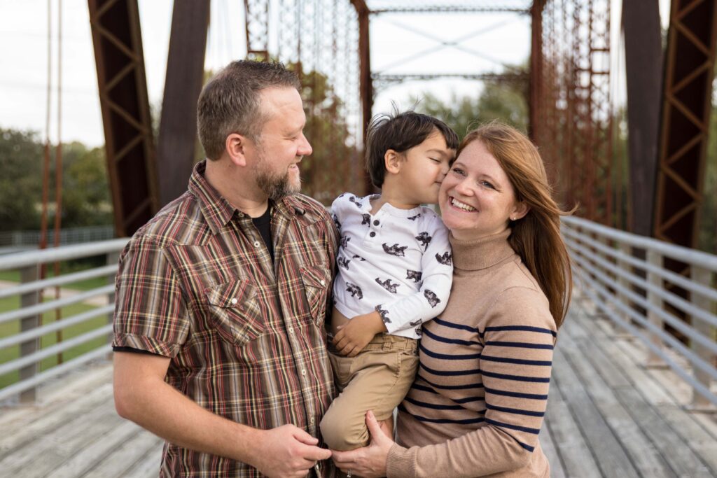 Austin family on the Richard Moya Bridge with parents holding boy and boy kissing the mom.