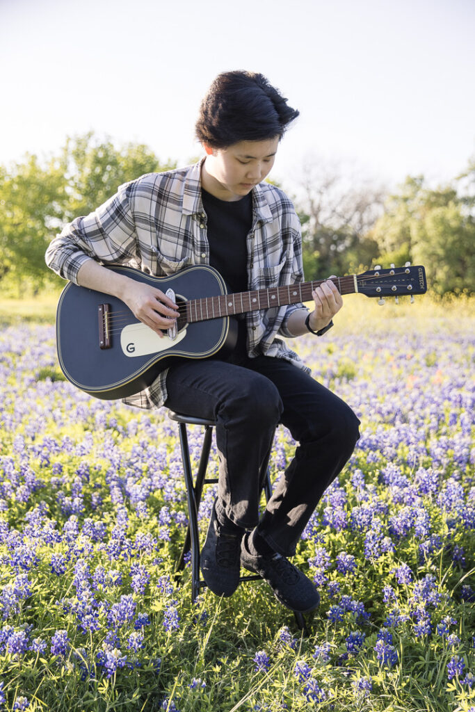 High school senior girl playing guitar in a bluebonnet field during her Austin senior. photography session