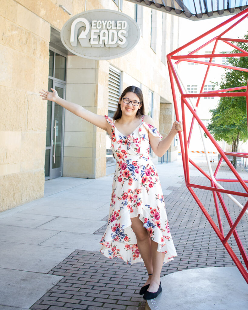 High school senior girl in a floral dress posing near a red geometric sculpture outside Austin Central Library.