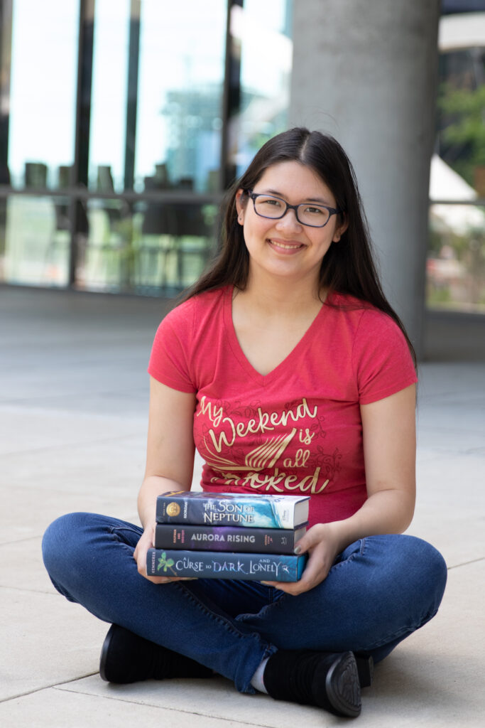 High school senior girl sitting with a stack of books outside Austin Central Library during her senior photo session.