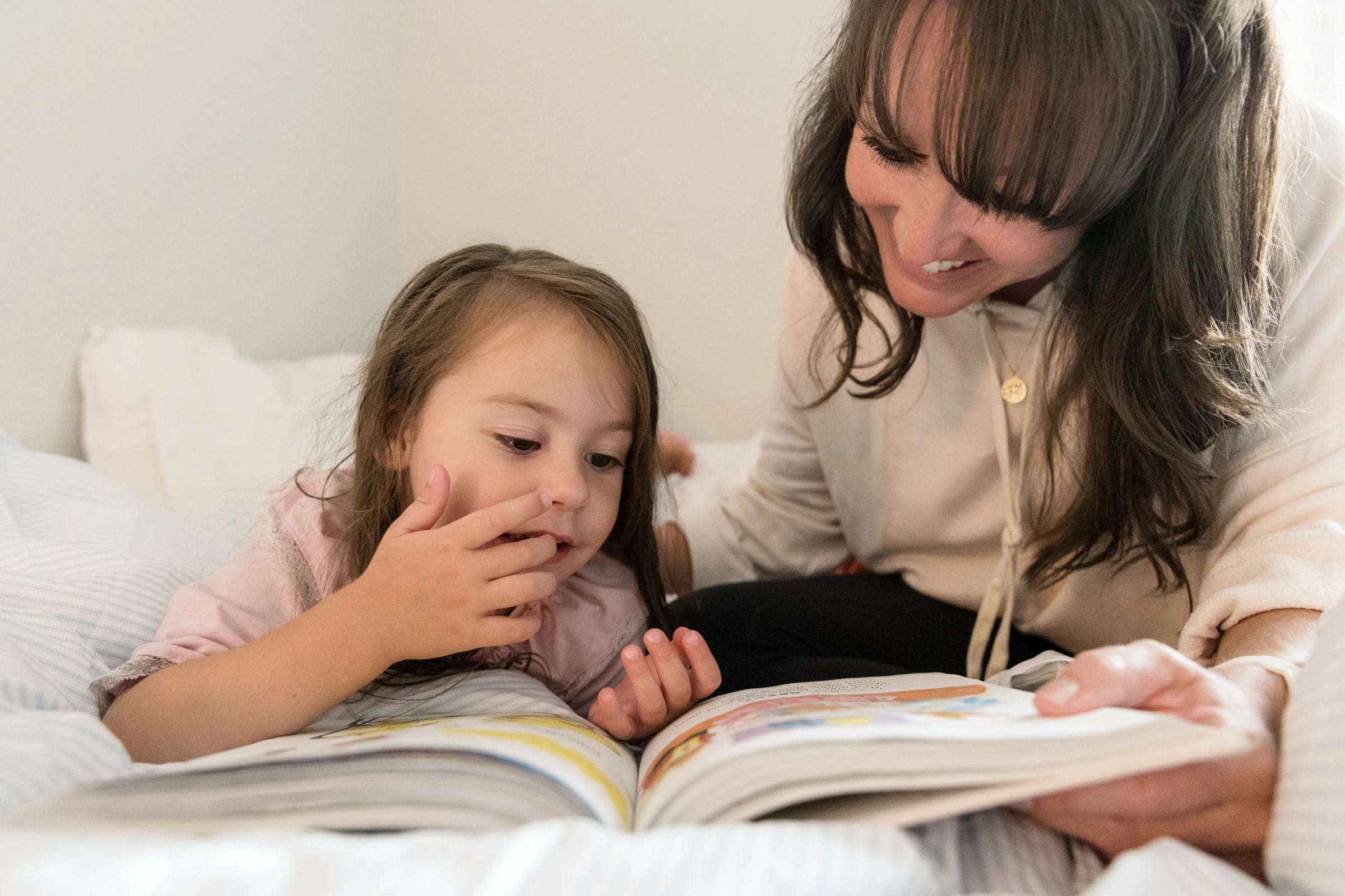 Parent and child reading a picture book together on a bed during a lifestyle family session in Austin