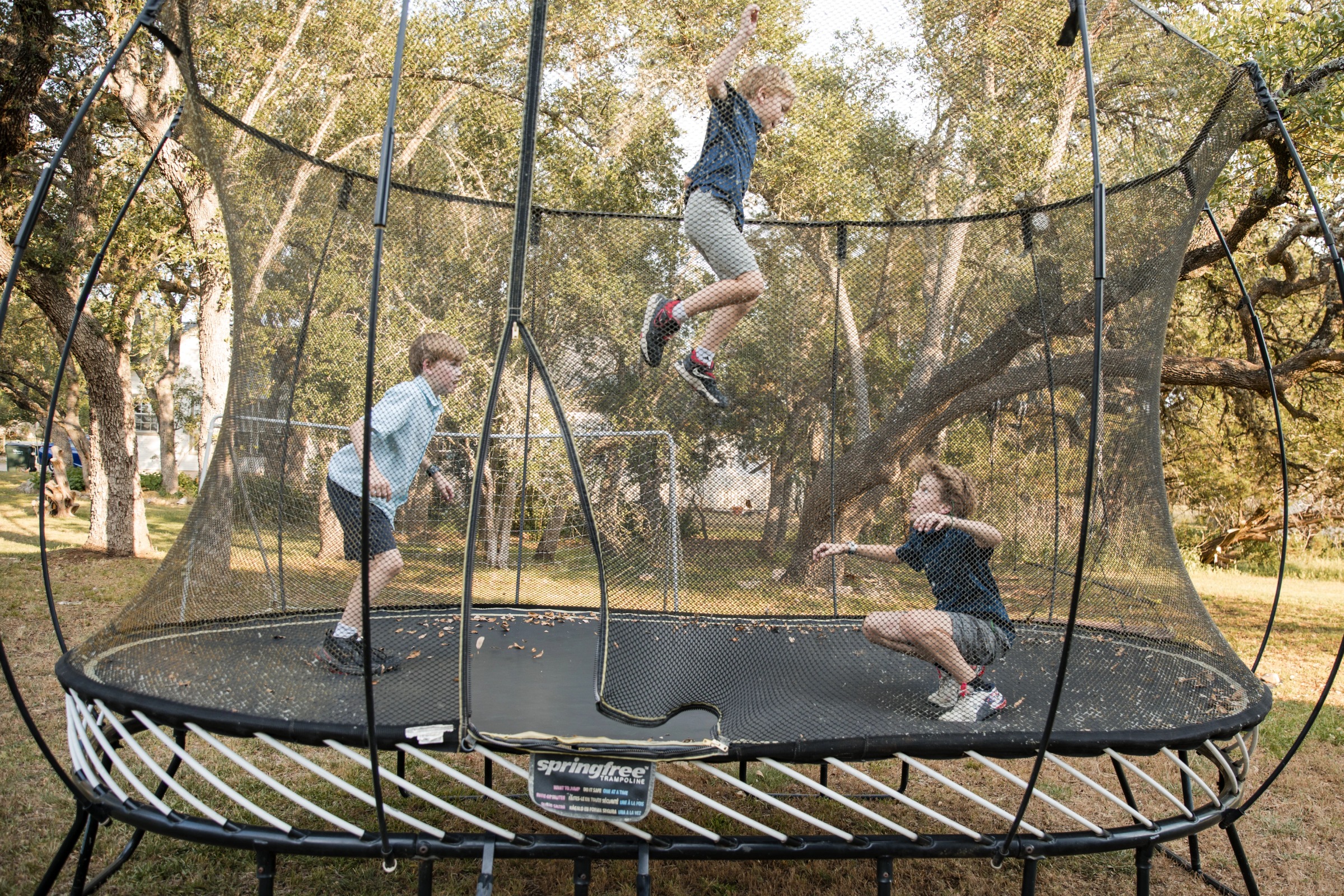 Two children bounce and play on a large outdoor trampoline, captured during a family session at a park in Austin