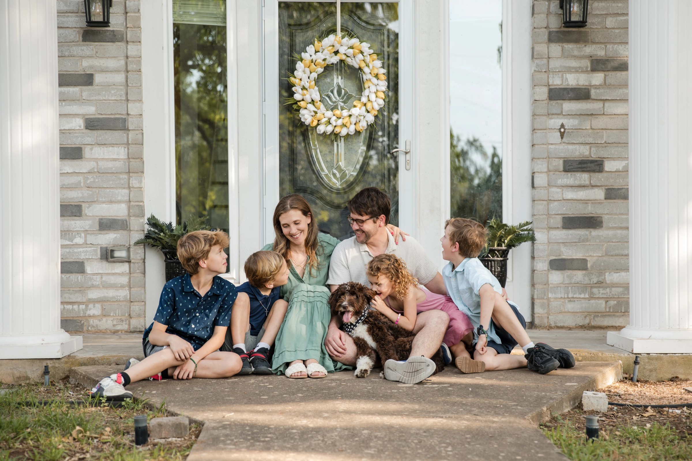 Mother and two children sit together on front porch steps during a family portrait session in Austin, TX